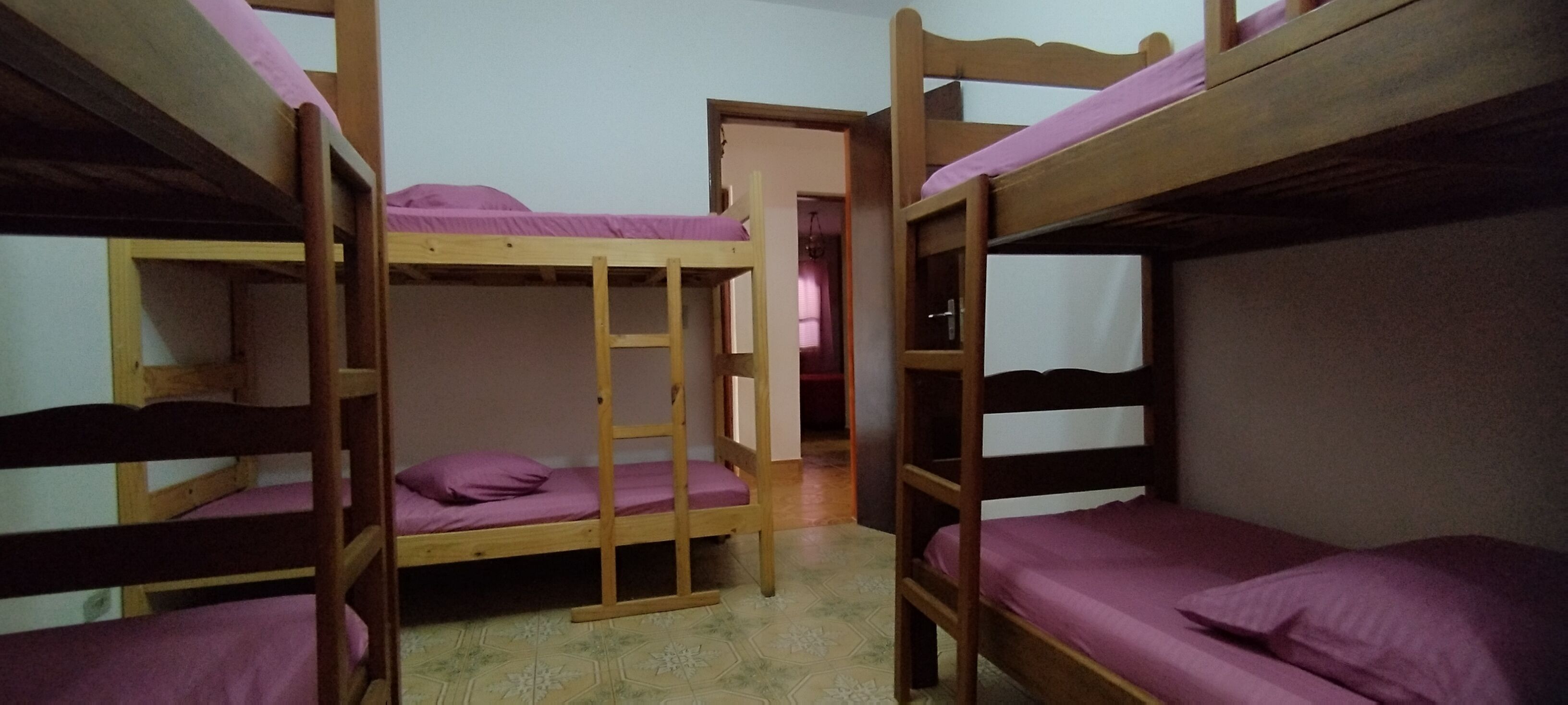 Een slaapkamer met stapelbed, een ladder, een houten hoofdbord en paars beddengoed.