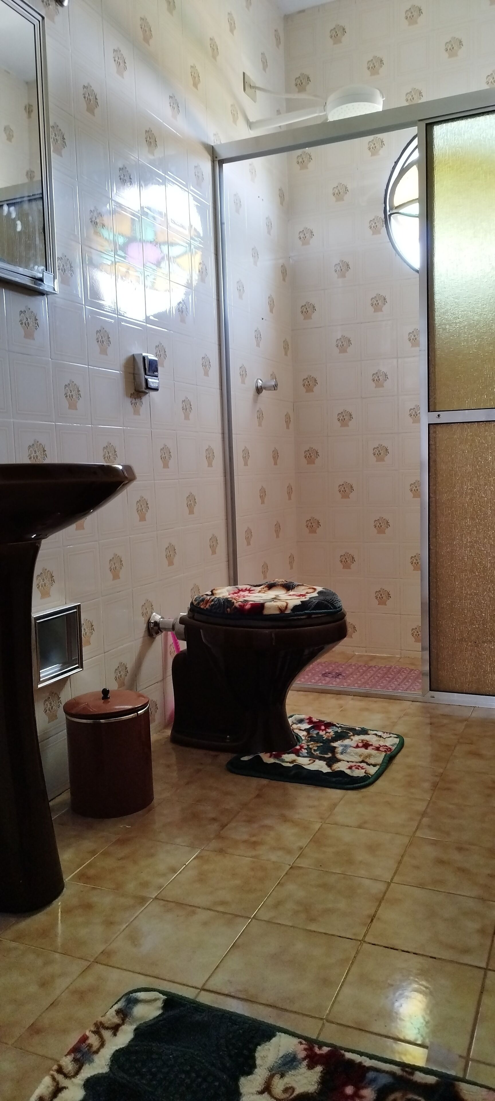 Ein Badezimmer mit gemusterten Fliesen, einer Toilette, einem Waschbecken, einem Spiegel und einem Fenster.