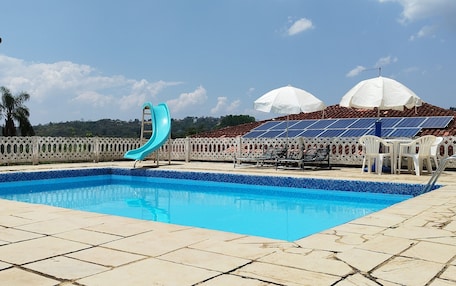 A swimming pool with a blue slide, white umbrellas, and solar panels on a roof.