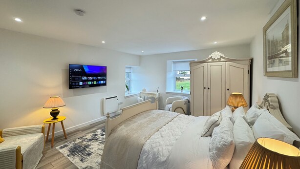 A modern bedroom with a bed, bedside lamps, a TV, and a wardrobe.