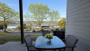 Un patio con una mesa y sillas, una planta en maceta y vistas a un lago y edificios al fondo.