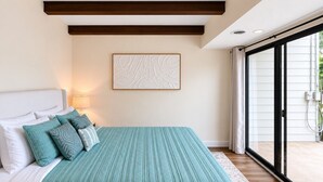 Un dormitorio con una cama, almohadas, una obra de arte colgada en la pared y un ventanal corredero que da a un espacio exterior.