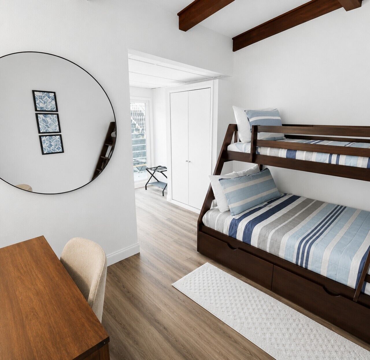 Un dormitorio con una cama litera, un espejo redondo, una mesa de madera y una silla.