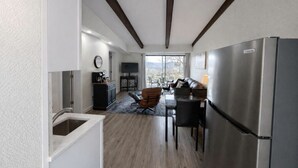 A modern kitchen with a stainless steel refrigerator, a dining area with a table and chairs, and a living room with a sofa and a TV.