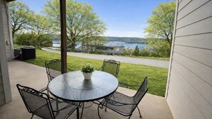 A covered patio with a round table and chairs, overlooking a grassy area and a body of water.