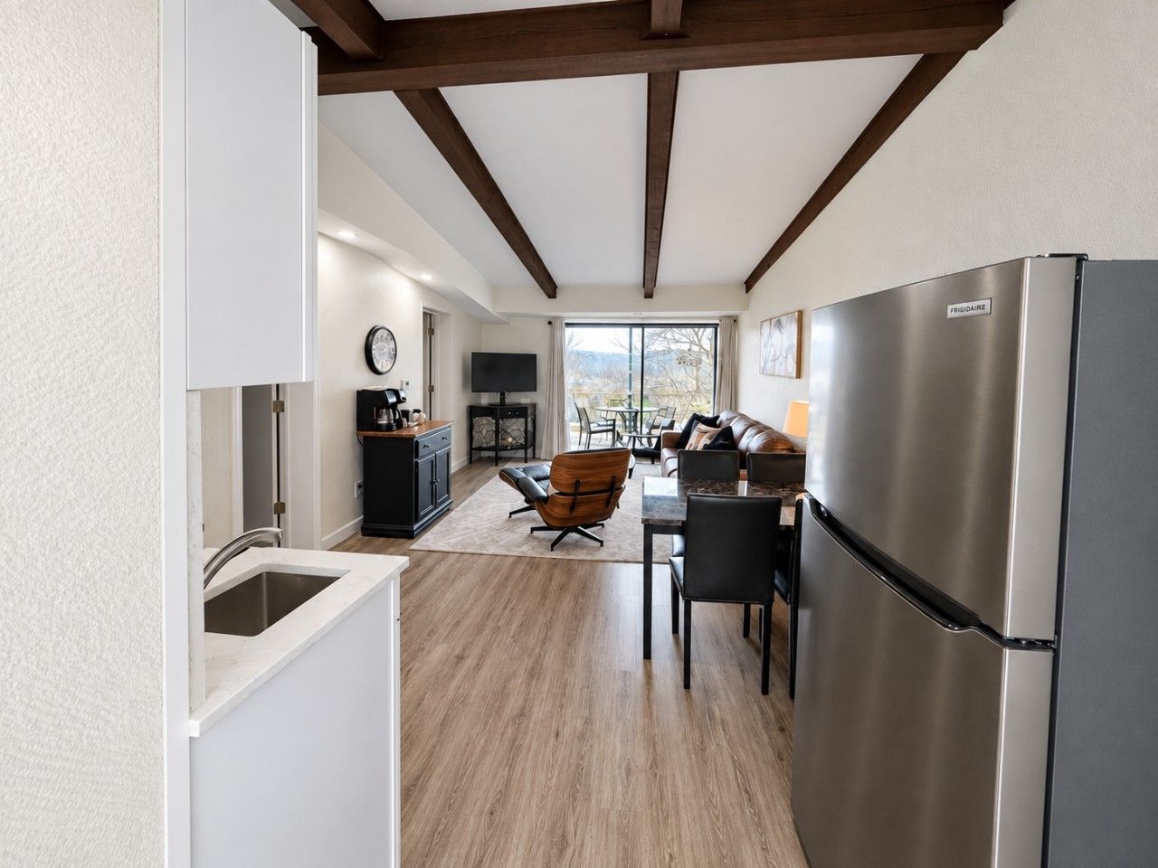 A modern kitchen with a stainless steel refrigerator, a dining area with a table and chairs, and a view through the window.