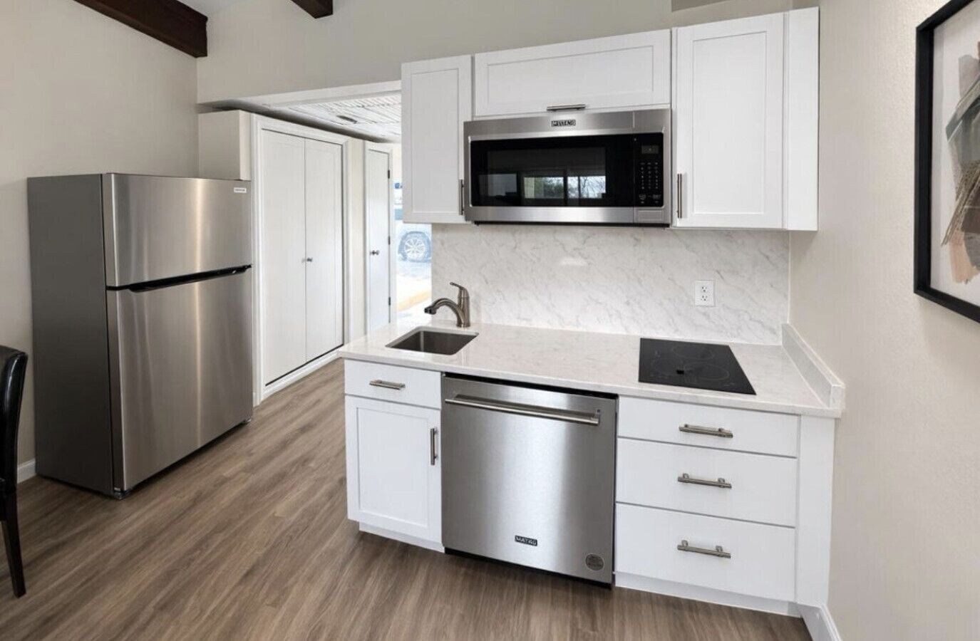 A modern kitchen with stainless steel appliances, white cabinetry, and a marble countertop.