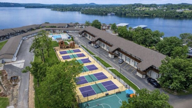 A hotel with multiple tennis courts, a swimming pool, and a view of a lake.
