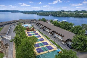 Ein Hotel mit mehreren Tennisplätzen, einem Schwimmbad und Blick auf einen See.
