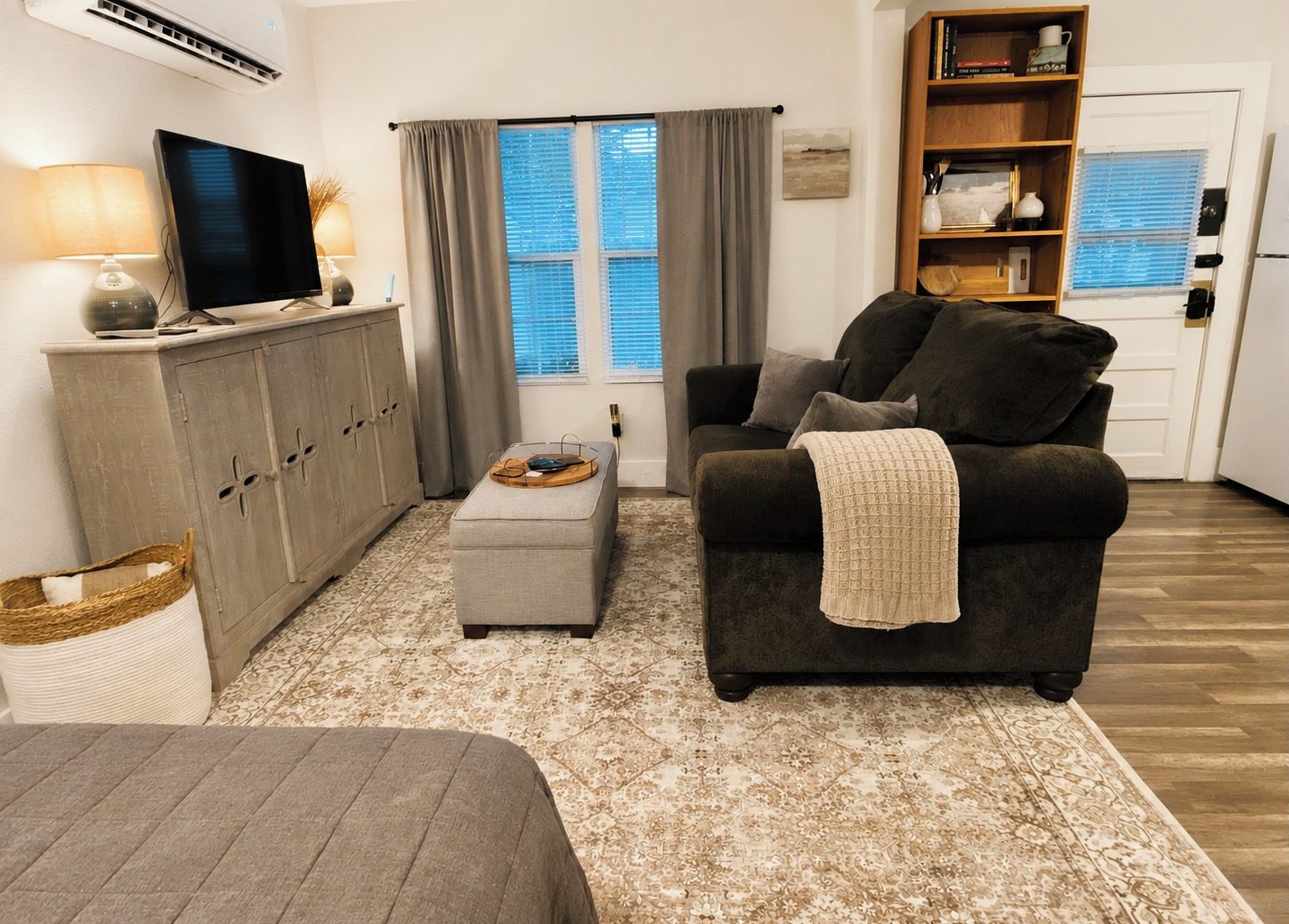 Un salon avec un canapé, un pouf et un téléviseur posé sur un meuble.