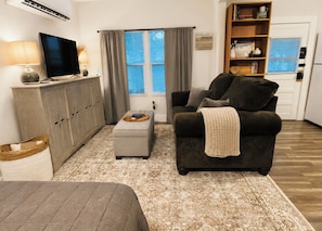 A living room with a sofa, ottoman, and a television on a cabinet.