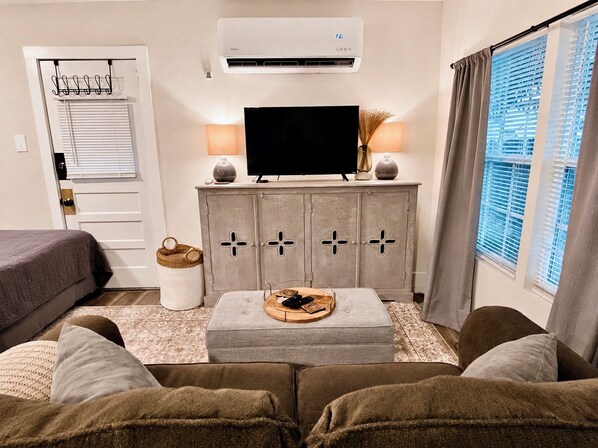 Una sala de estar con sofá, reposapiés, televisor y aparador.