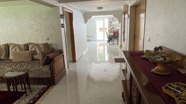 A spacious living area with a sofa set, a coffee table, and a decorative table with a vase. A hallway leads to a bright room with a door. - House (level1) 10 mn beach Mehdia Kénitra in magnificent villa peaceful calm (Kénitra)