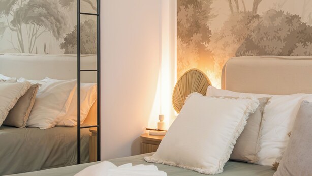 A hotel room with a bed, pillows, a mirror, and a wall mural.