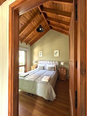 Une chambre avec un plafond en pente, un lit doté d’une tête de lit, deux tables de chevet avec des lampes et des œuvres d’art encadrées accrochées au mur.