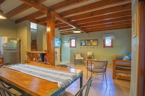 A cozy room with a wooden table, chairs, a bed, a refrigerator, and a staircase leading to another level.