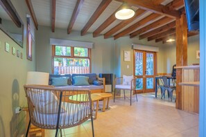 A spacious living area with a wooden ceiling, a sofa, chairs, a dining table, and a view through a glass door.