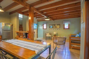 Ein gemütliches Zimmer mit Holztisch, Stühlen, einem Bett, einem Kühlschrank und einer Treppe zu einer weiteren Ebene.