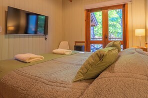 A room with a bed, a TV mounted on the wall, a window with a view of trees, and a door.