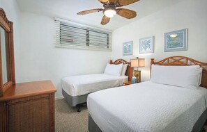 Une chambre avec deux lits simples, un ventilateur de plafond, une table de chevet avec une lampe et un miroir fixé au mur.