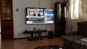 Un salon avec un téléviseur fixé au mur diffusant un bulletin d’information, un canapé à motifs et un meuble en bois.