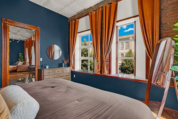 Une chambre avec un grand lit, une commode, un miroir et une fenêtre avec des rideaux.