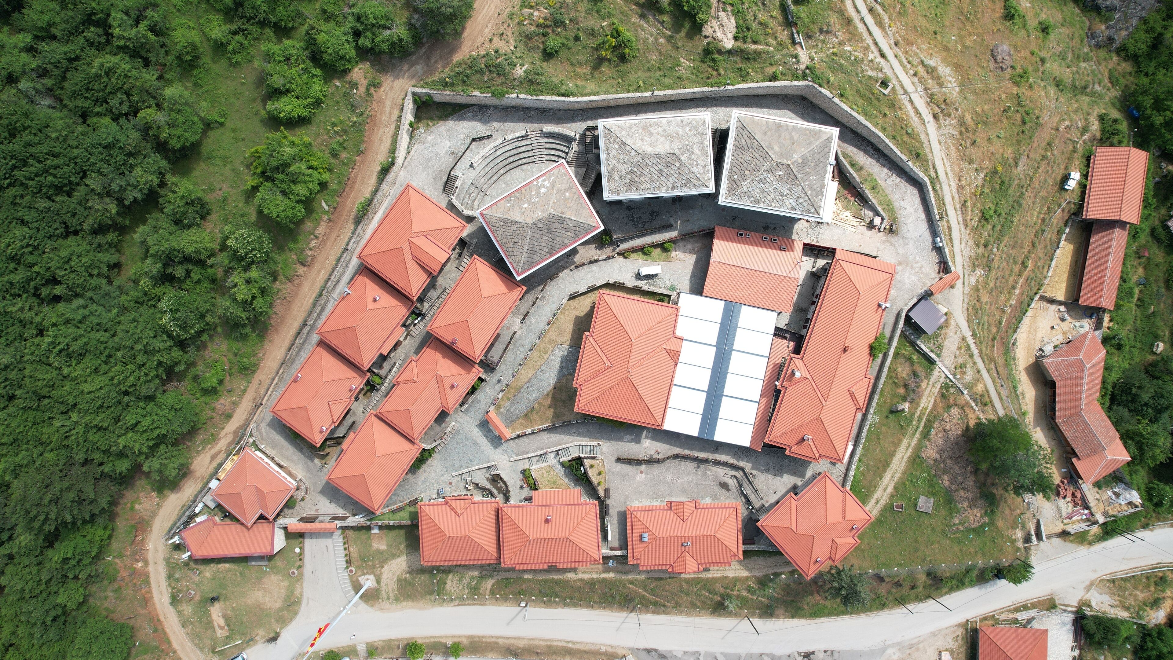 An aerial view of a large complex with multiple buildings, including a central structure with a large white facade and surrounding buildings with red roofs.