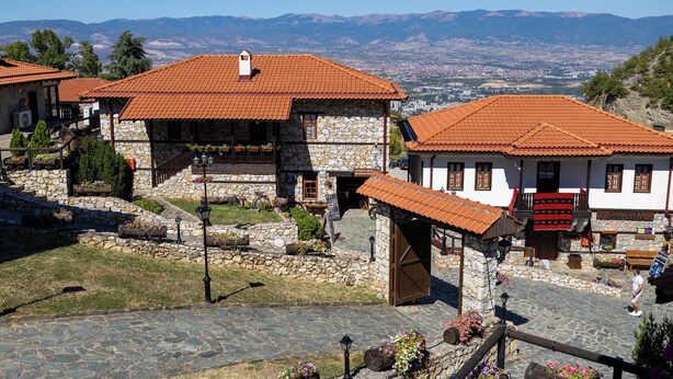 Un edificio de piedra con techo de tejas rojas, una escalera de piedra y vistas a montañas distantes.