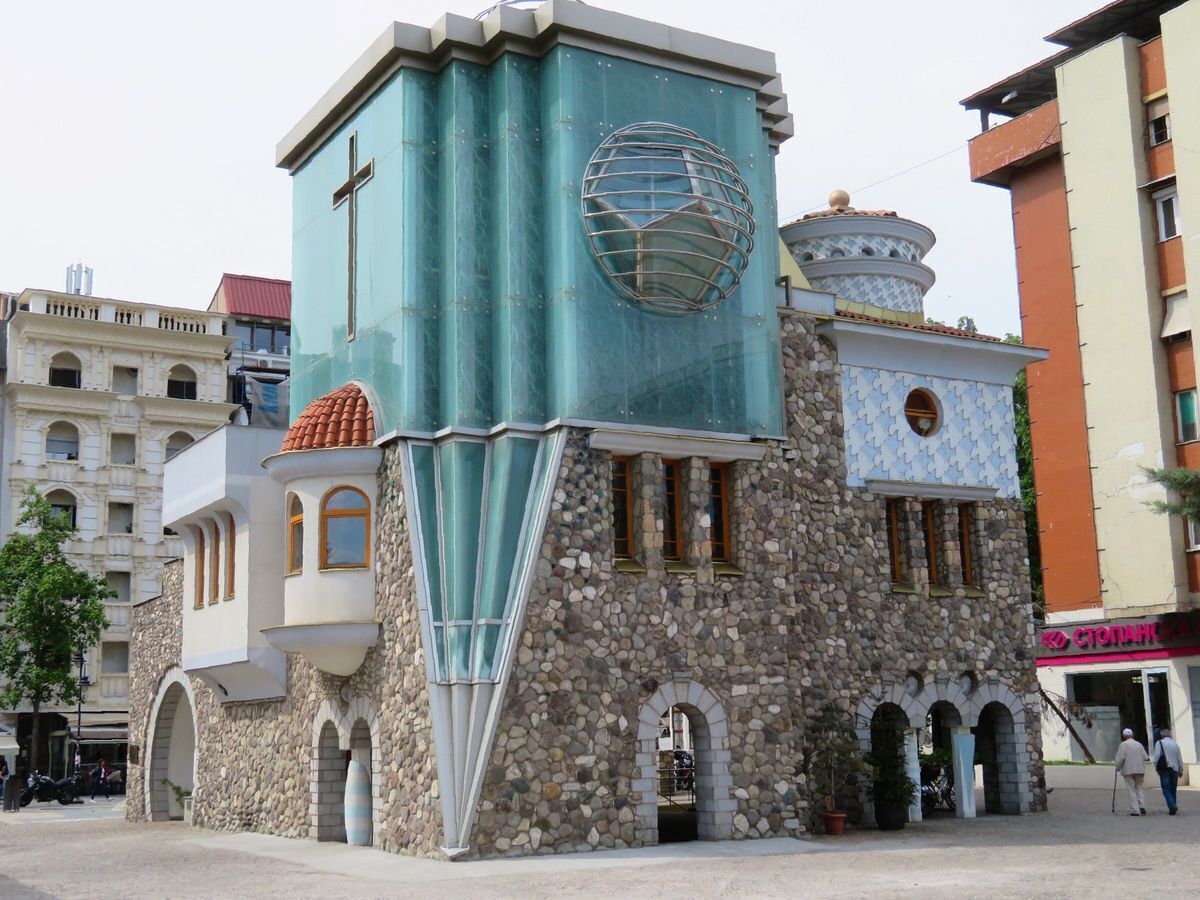 A unique building with a stone facade, a prominent cross, and a spherical glass structure.