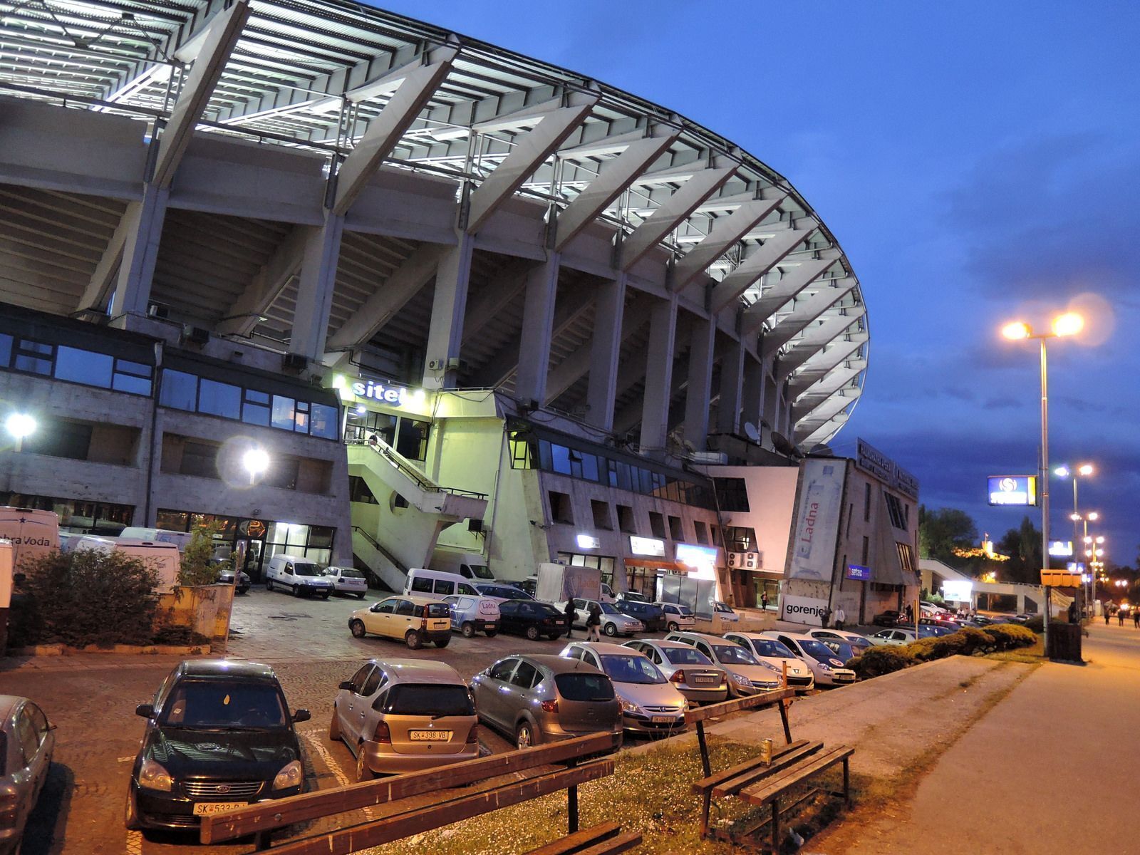 Un estacionamiento con automóviles y un estadio al fondo.