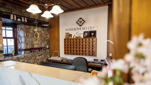 Zona de recepción con pared de piedra, estantes de madera, mostrador de mármol y una exhibición de objetos enmarcados.