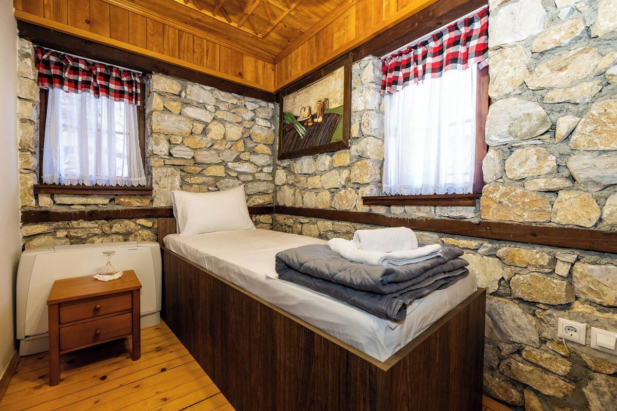 Une chambre avec un mur en pierre, un plafond en bois et un lit avec des oreillers et une couverture.