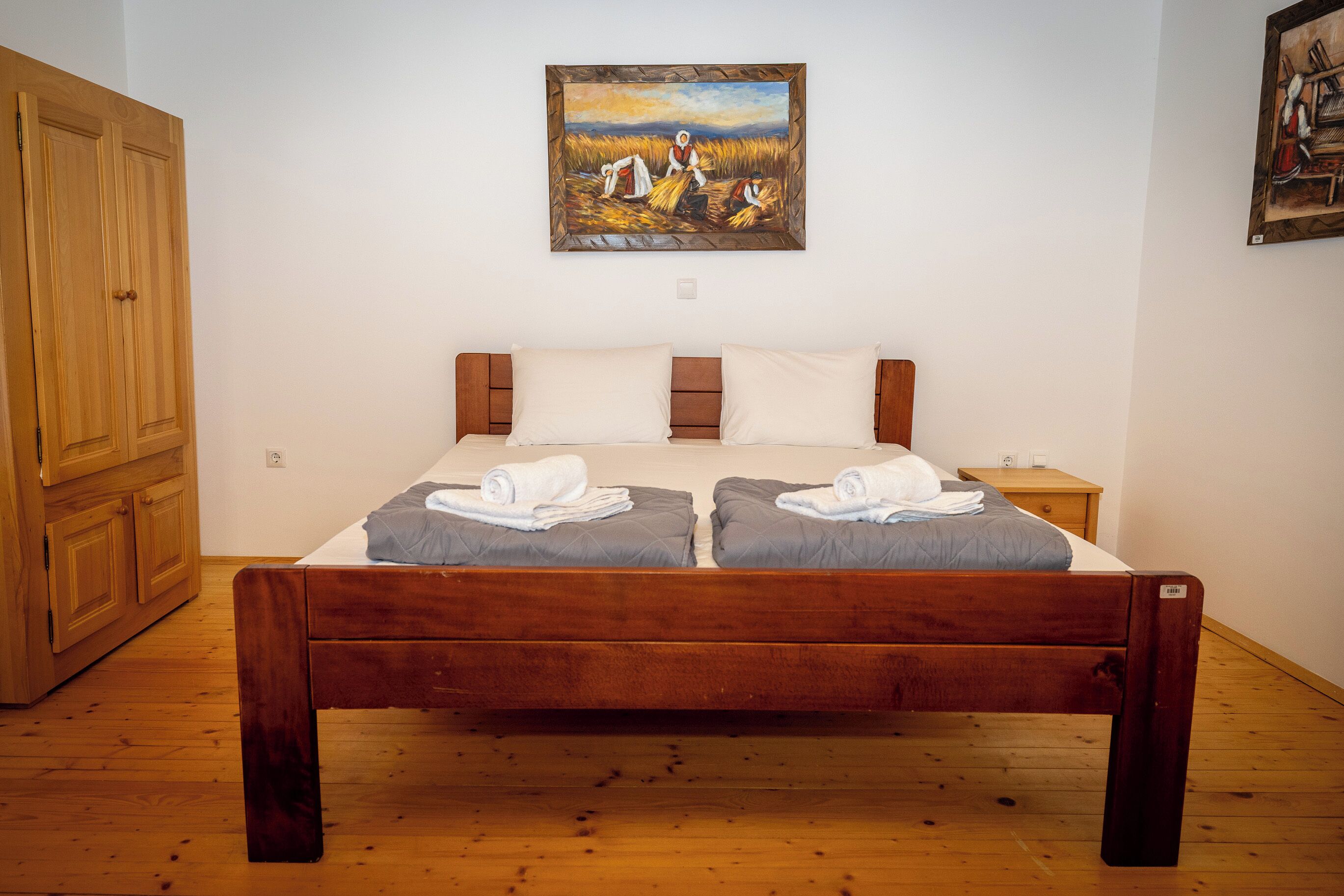 A double bed with two pillows, a wooden headboard, a wooden wardrobe, and a painting on the wall.
