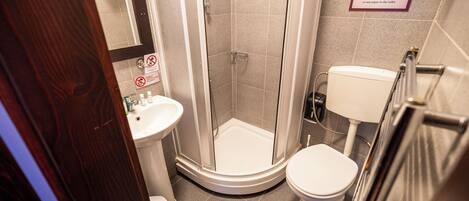 A bathroom with a shower, toilet, and sink. There are signs indicating no flushing of toilet paper and no water wastage.