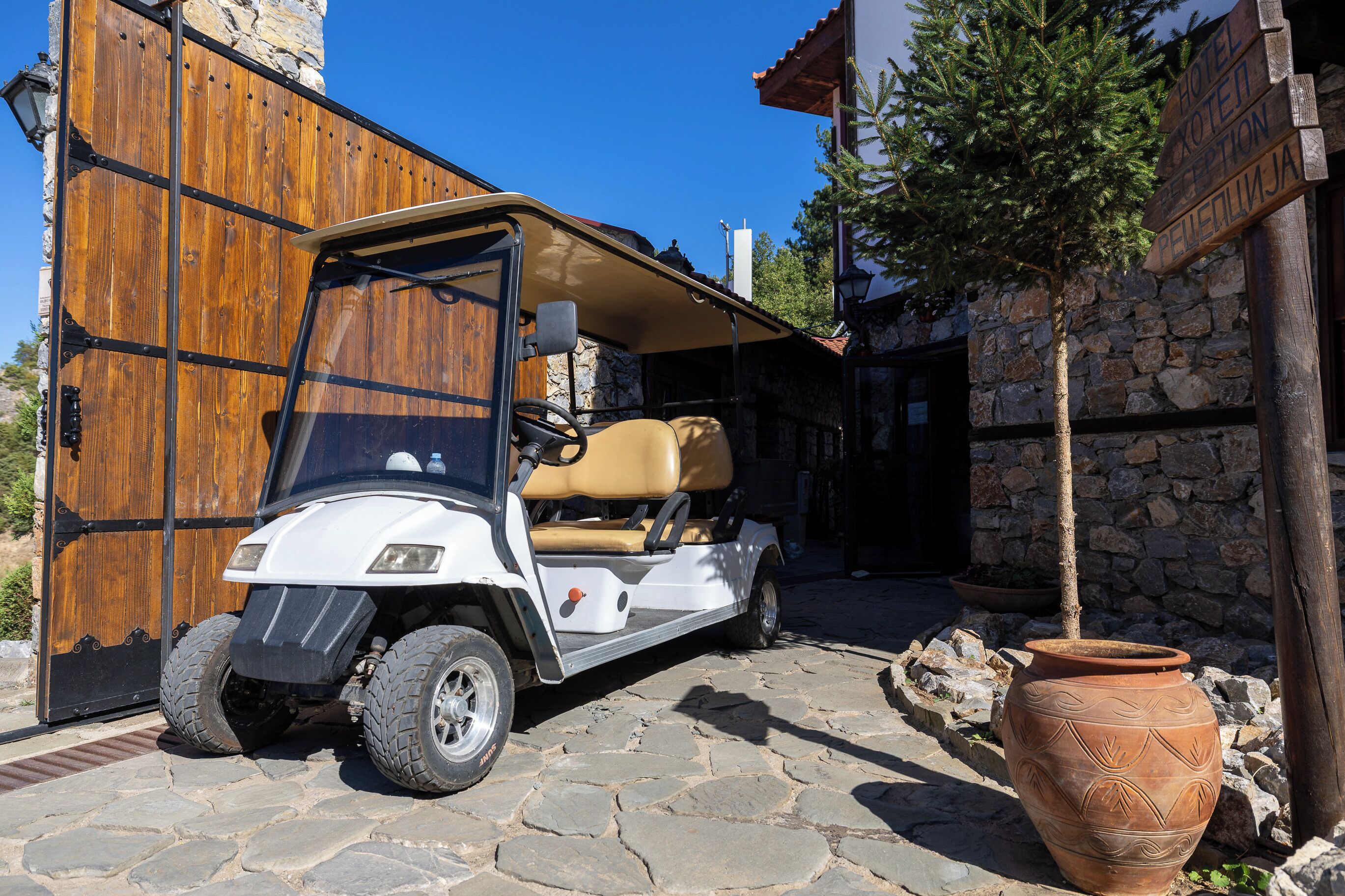 A golf cart parked in front of a stone building with a wooden door and a sign indicating a hotel.
