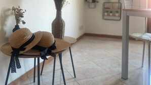 Un coin de pièce avec une chaise, un vase contenant des plantes séchées et des tableaux encadrés accrochés au mur.