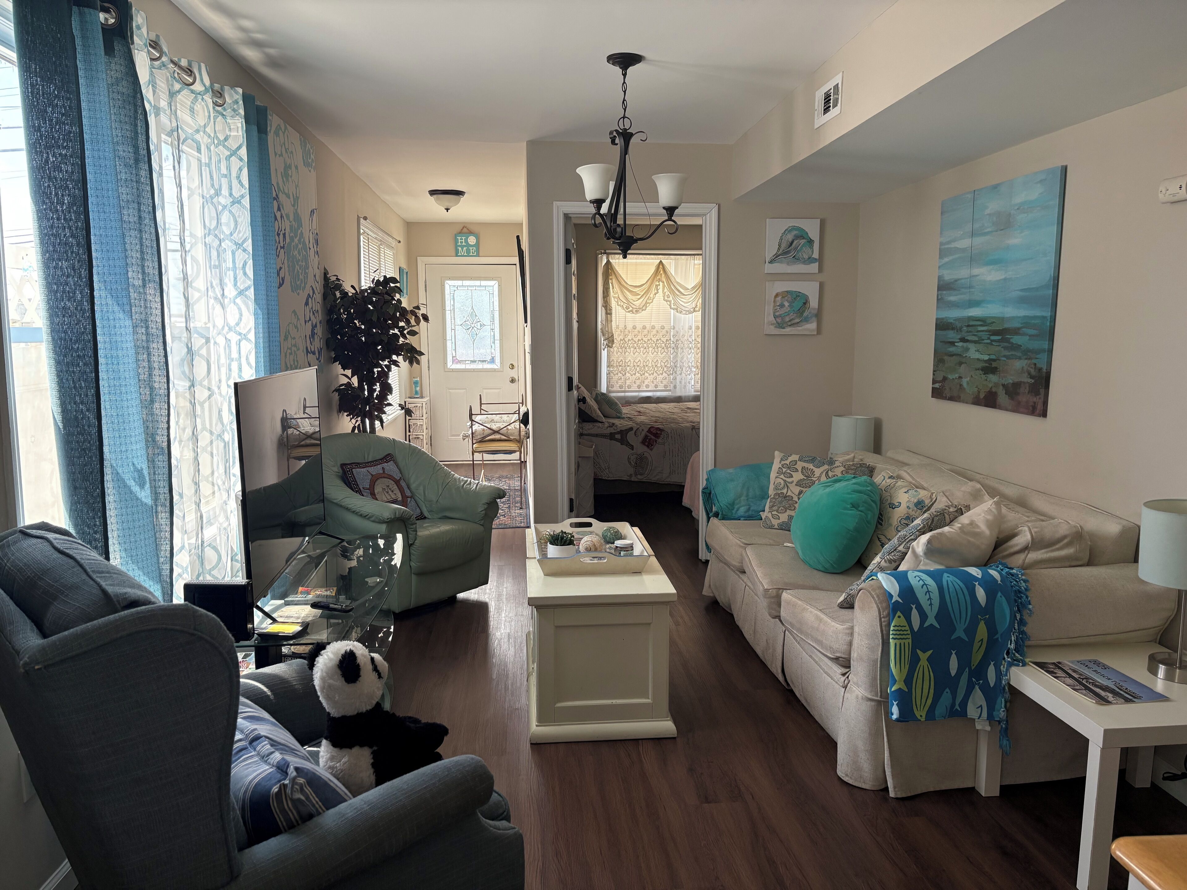 A living room with a sofa, armchair, and a coffee table. There is a plant, a lamp, and artwork on the walls.
