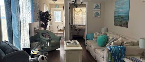 A living room with a sofa, armchair, and a coffee table. There is a plant, a lamp, and artwork on the walls.