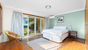 Un dormitorio con cama, una silla, un escritorio y vistas a través de un ventanal corredera.