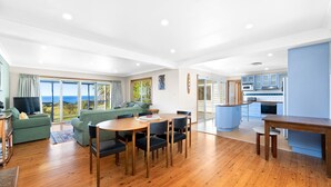 Una sala de estar moderna con comedor, cocina y puerta corrediza de vidrio que da a un balcón con vista al mar.