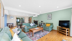 Un salón amplio con un sofá verde, una mesa de centro de madera y un televisor sobre un mueble de madera.