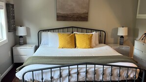 Une chambre à coucher avec un lit en métal, un tapis à motifs, deux tables de chevet avec des lampes et un tableau au mur.