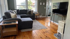 Un salon comprenant un canapé d’angle, un pouf, une table basse en bois et un téléviseur posé sur un meuble.