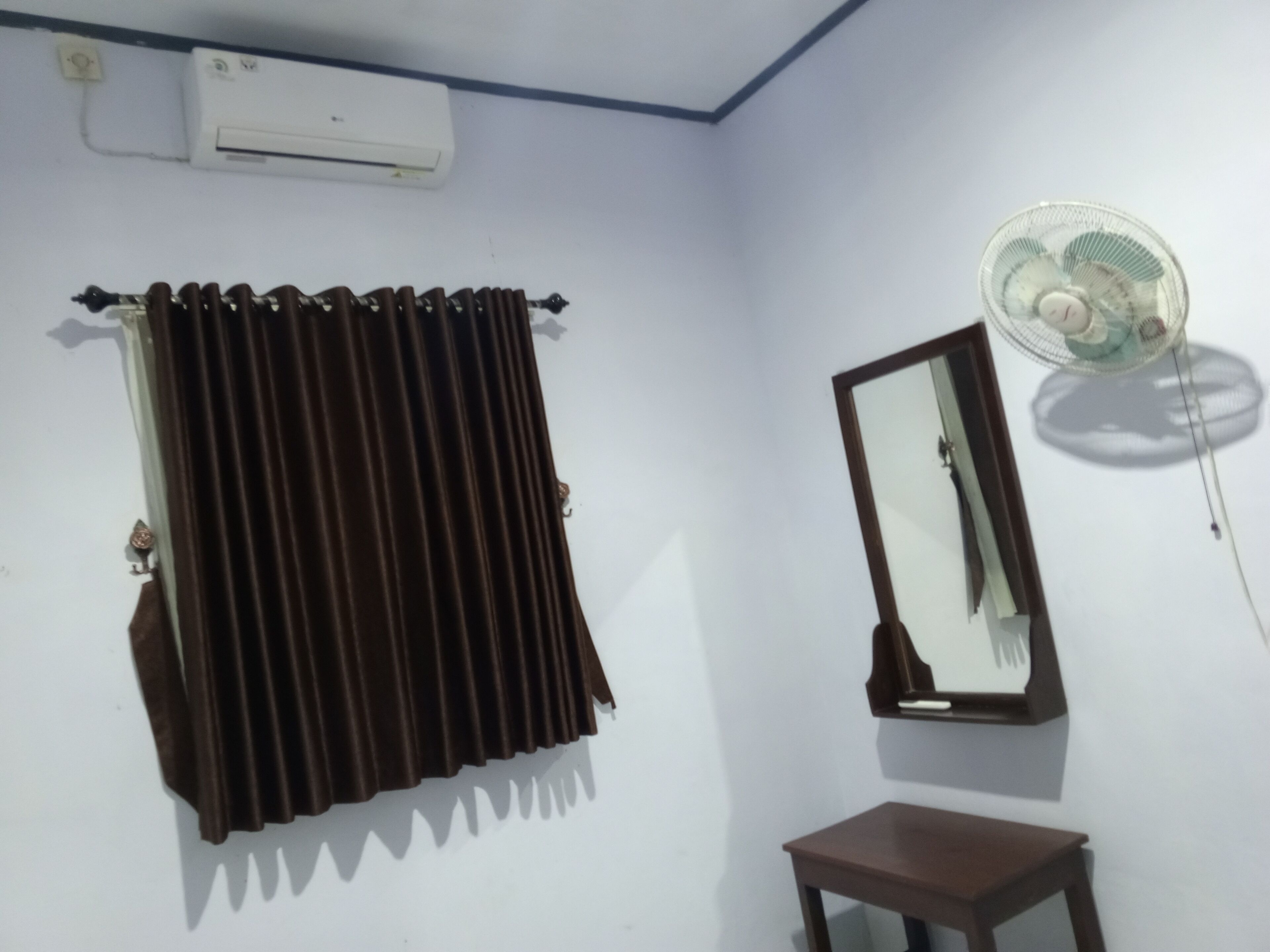 A room with a curtain, a fan, a mirror, and a small table.