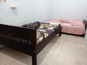 A bedroom with two beds, one with a patterned bedspread and the other with a striped bedspread. - Nirmala Homestay  (Sarongan)