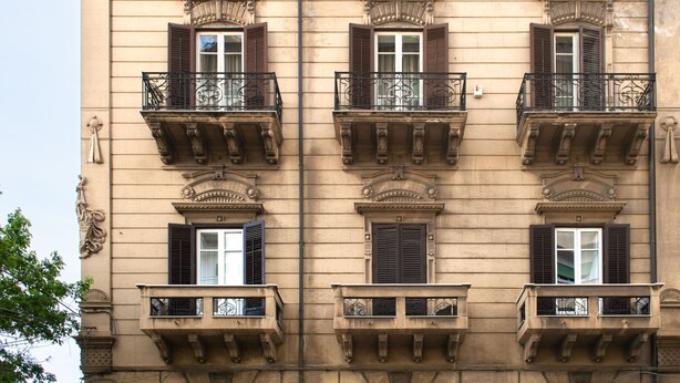 Un edificio con varios balcones, cada uno con barandillas de hierro forjado y contraventanas.