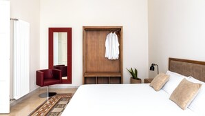 Un dormitorio con cama, un armario de madera, una silla roja, un espejo y una mesita de noche con lámpara.