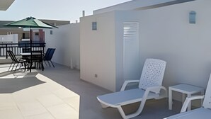 A sunlit outdoor patio with white walls, a table with chairs, and two lounge chairs. - Condo with Rooftop steps from the beach! (Punta Cana)