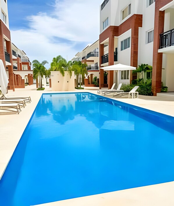 Ein Swimmingpool mit Liegestühlen und Sonnenschirmen, umgeben von mehrstöckigen Gebäuden mit Balkonen.