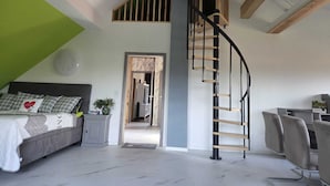 Quarto moderno com teto estilo loft, escada curva, cama com cabeceira, escrivaninha e uma cadeira.